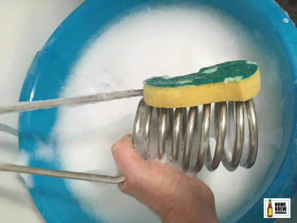 A stainless steel wort chiller being cleaned by hand with warm soapy water