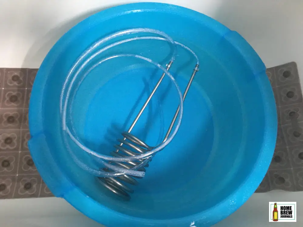A stainless steel wort chiller soaking in clean water in a large blue washing up bowl