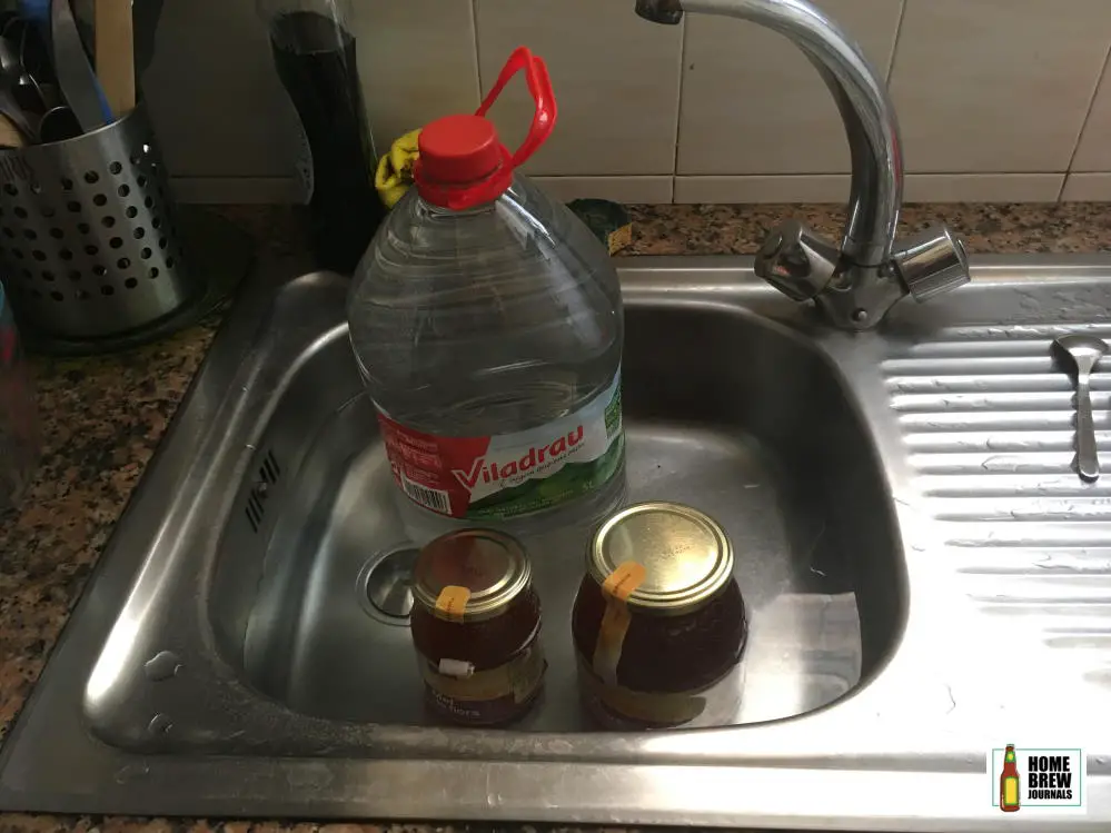 Two jars of honey and a bottle of spring water in a sink full of hot water, part of the mead making process